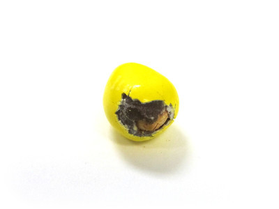 A big yellow nut candy, with a big continent of chipped shell, facing you. The nut peeks out, below.