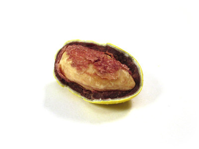 A yellow nut, with half the shell off, open-faced. Some brown papery peanut skin is smattered across the top.